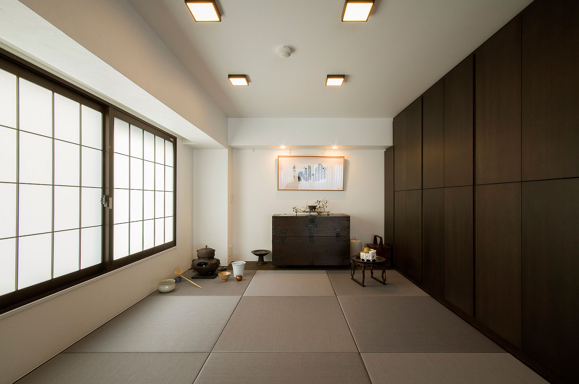 施工写真。縁なし畳が敷き詰められた和のスペース。左手の障子窓から自然光が入り、正面には時代箪笥とその上に飾られた絵画が見える。右手は一面がダークブラウンの壁面収納になっており、左奥には茶釜などの茶道具が配置されている。